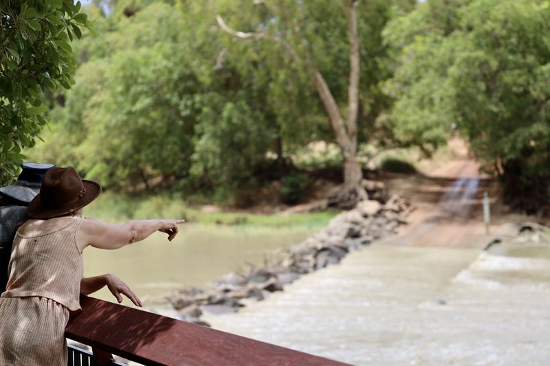 2 people wearing hats look away over the tree-lined river at Cahills Crossing from the newly built lookout. Credit Parks Australia.