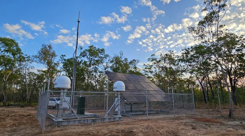 Mobile signal infrastructure in a fenced-off outdoor area of Kakadu. Several short, white domed towers and a large angled panel are within the fence permiter.