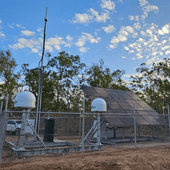 Mobile signal infrastructure in a fenced-off outdoor area of Kakadu. Several short, white domed towers and a large angled panel are within the fence permiter