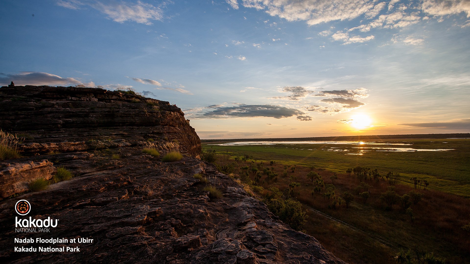 A large rocky cliff looks out over wetlands as the sun sets, at Nadab floodplain at Ubirr